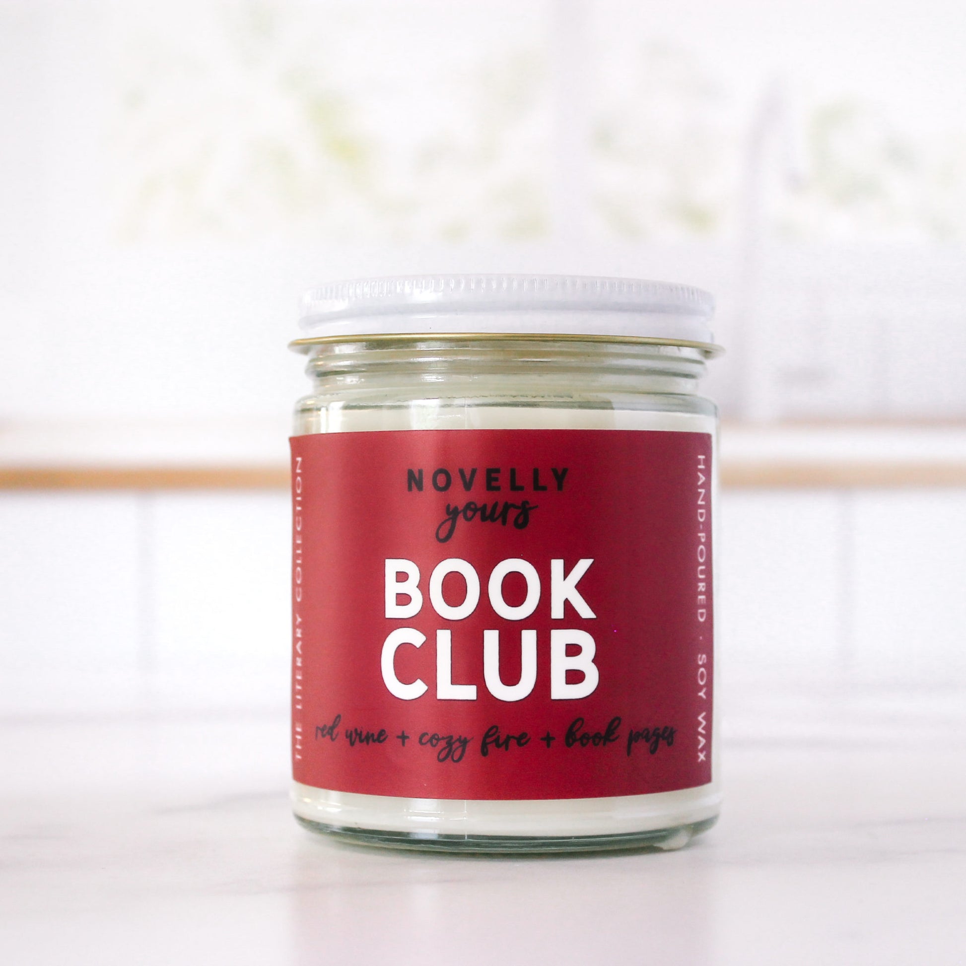 book-inspired "Book Club" candle with wine red label sits in front of red brick background