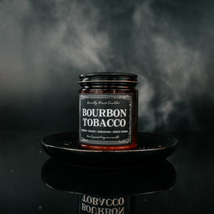 bourbon tobacco named candle in amber glass jar with black lid, sits on top of black tray against black smoky background
