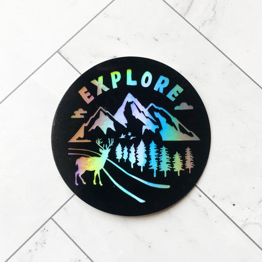 holographic sticker with word "explore" and nature designs of mountains, pine trees, and deer