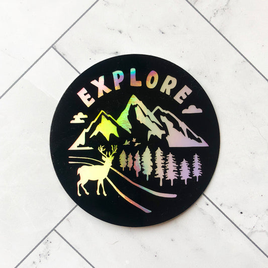 holographic sticker with word "explore" and nature designs of mountains, pine trees, and deer