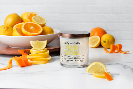 fresh citrus soy wax candle with yellow text in clear glass tumbler with bronze lid. surrounded by oranges and lemons.