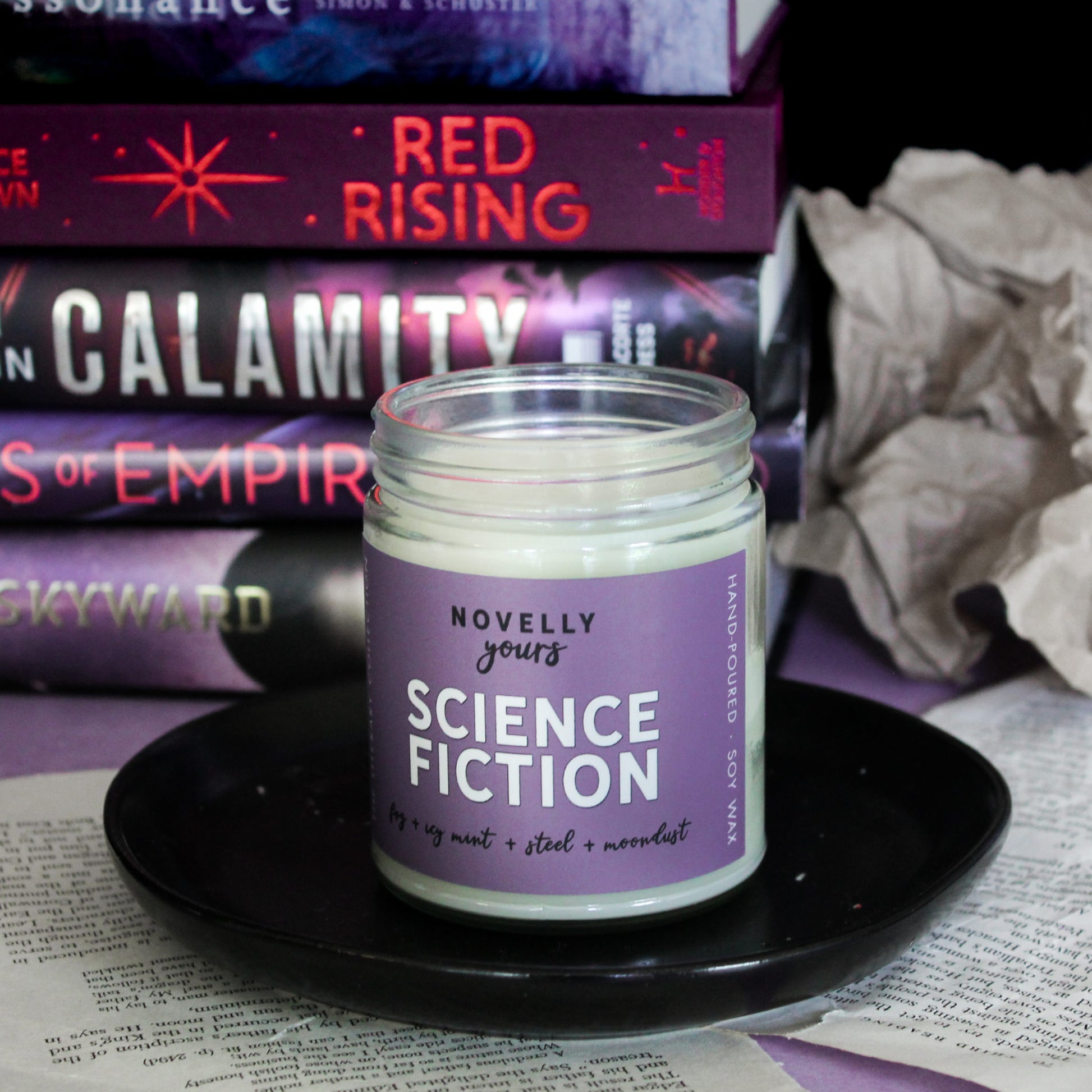 scented soy wax candle labeled "Science Fiction" sitting on on a black saucer in front of a stack of sci-fi books