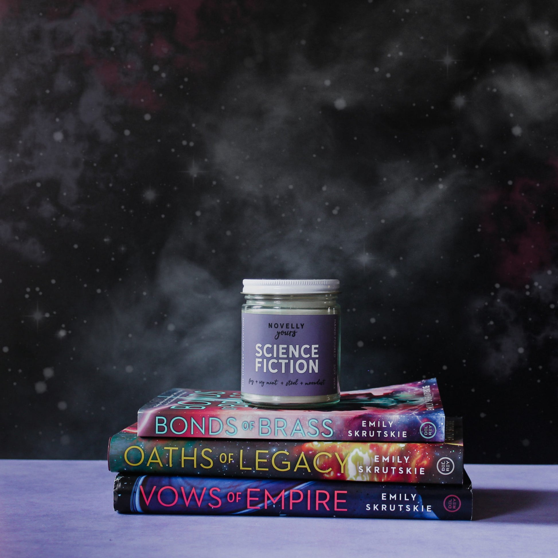 scented soy wax candle labeled "Science Fiction" sitting on top of a stack of sci-fi books. The background is black with stars on a purple base.