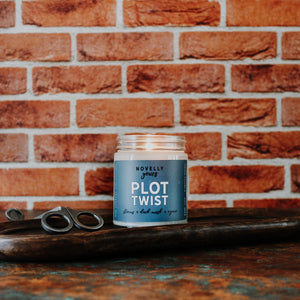 candle for bookworms, scented book candle Plot Twist with medium blue label and red brick background