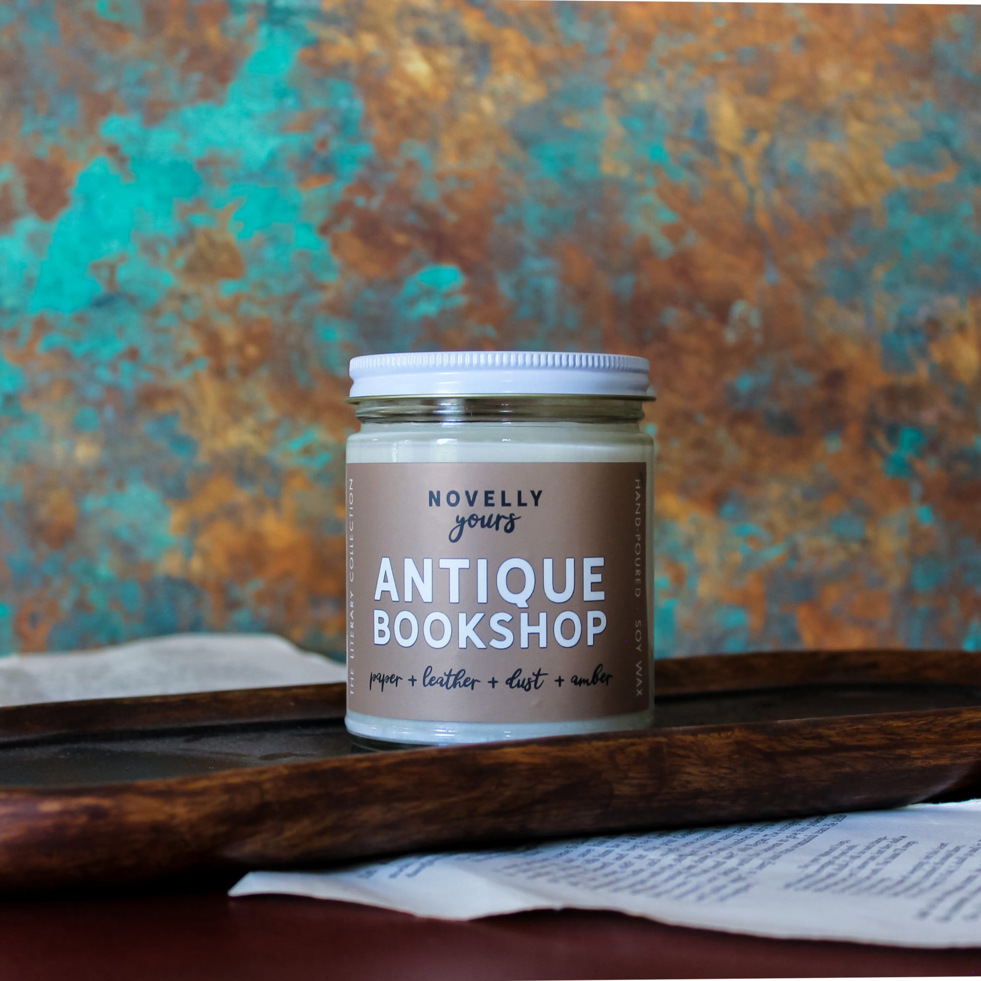 book inspired candle "Antique Bookshop" with beige label sits in front of rustic background surrounded by book pages