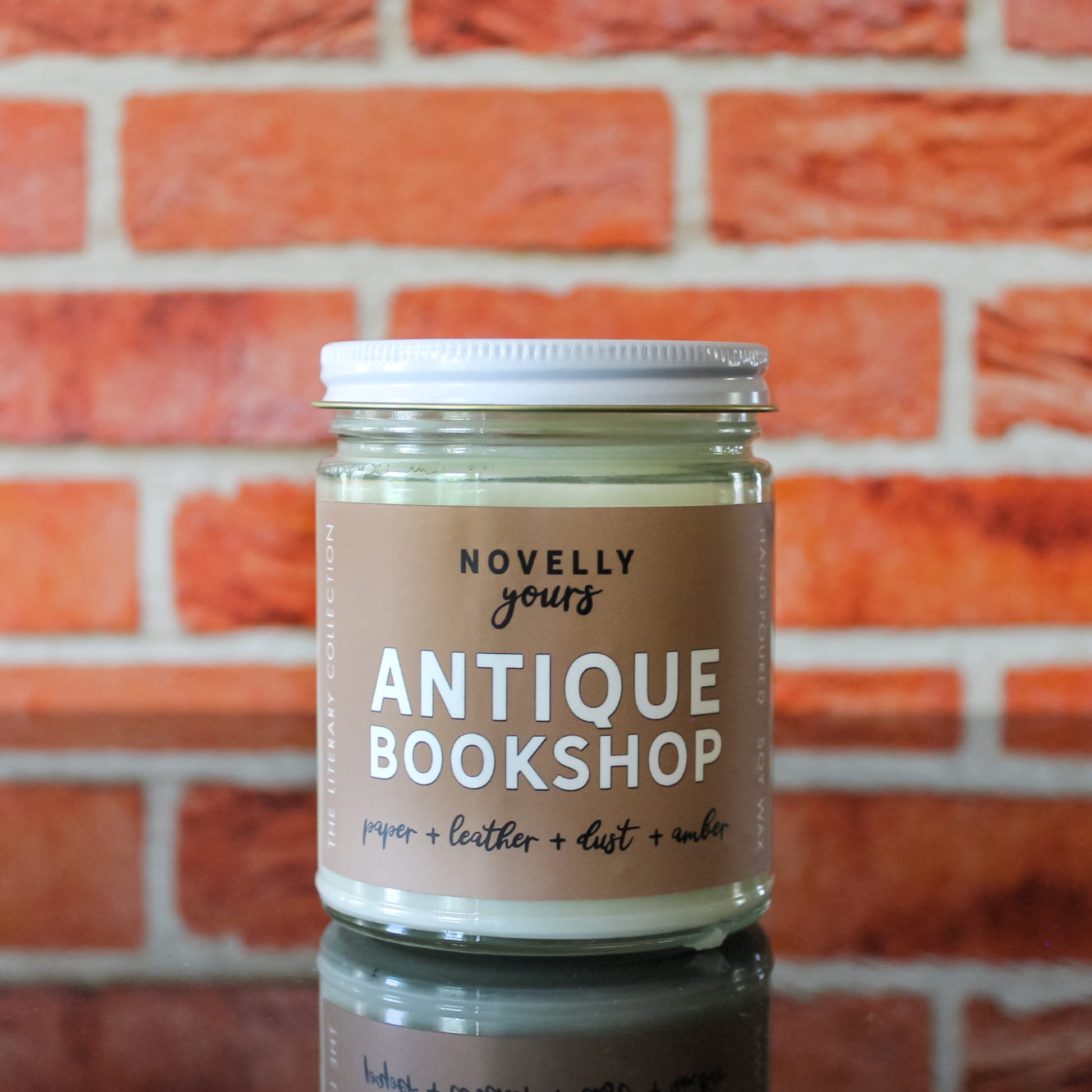 book inspired candle "Antique Bookshop" with beige label sits in front of red brick background