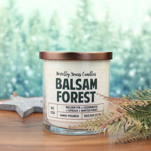 scented candle with balsam forest title in clear jar with bronze lid against pine tree background