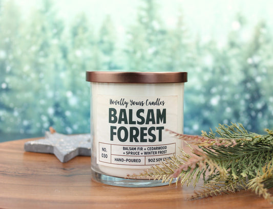 scented candle with balsam forest title in clear jar with bronze lid against pine tree background