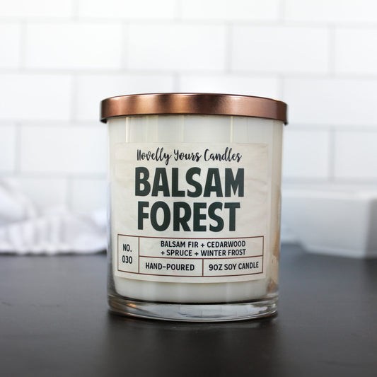scented candle with balsam forest title in clear jar with bronze lid against white tile background