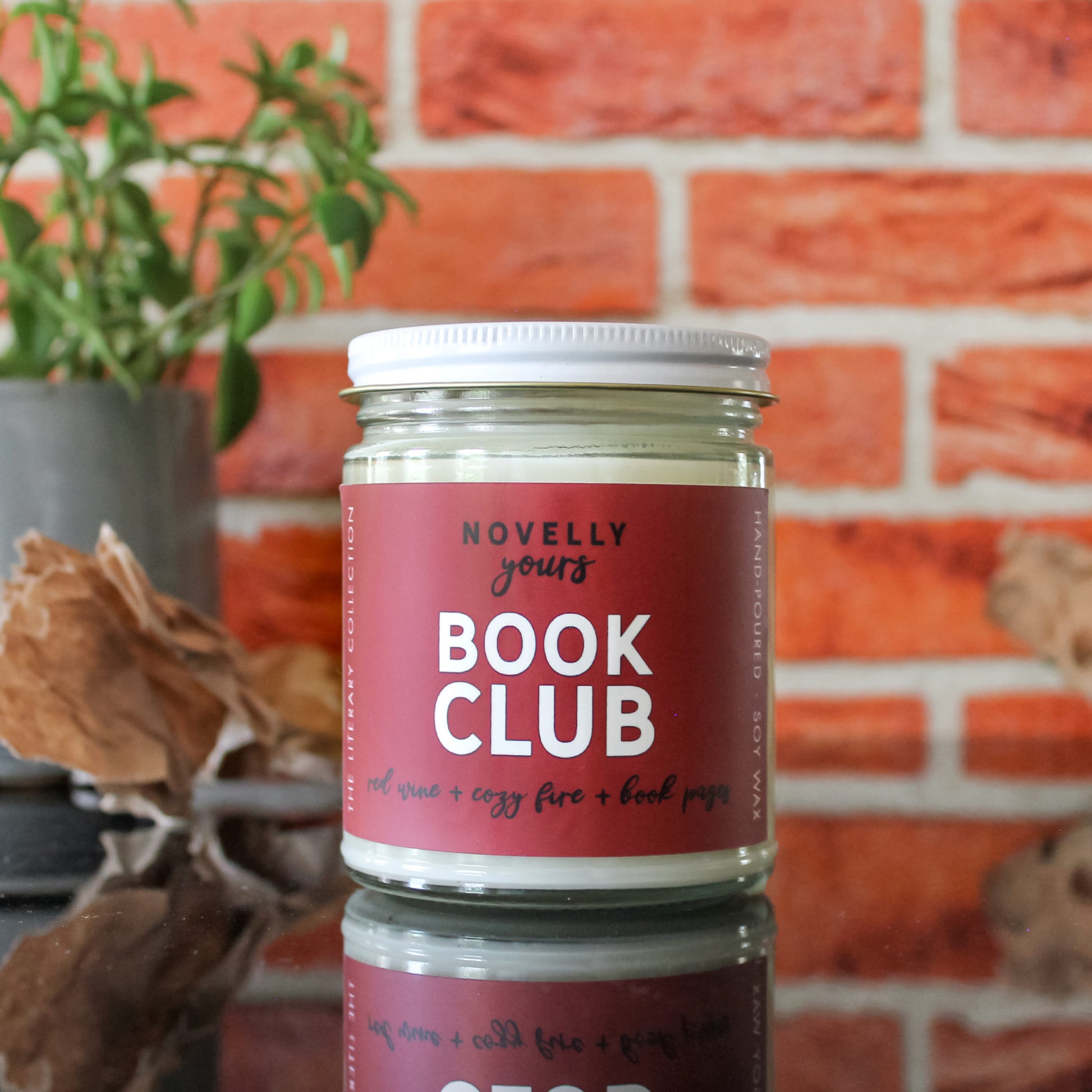 book-inspired "Book Club" candle with wine red label sits in front of red brick background