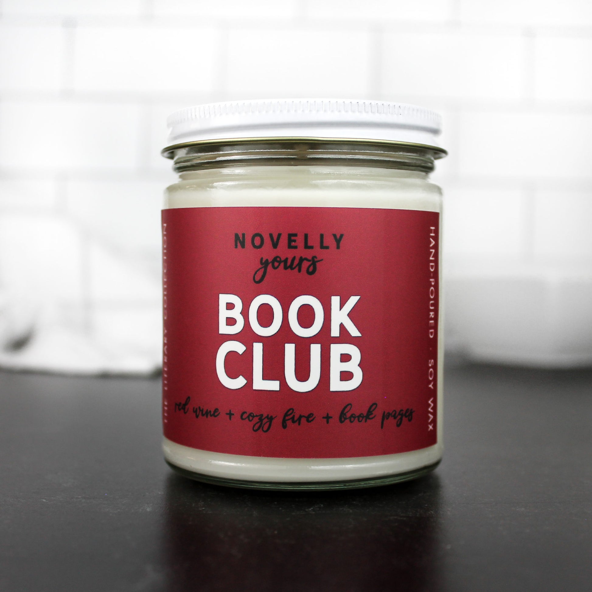 scented soy wax candle called book club on red wine label in clear jar with white lid