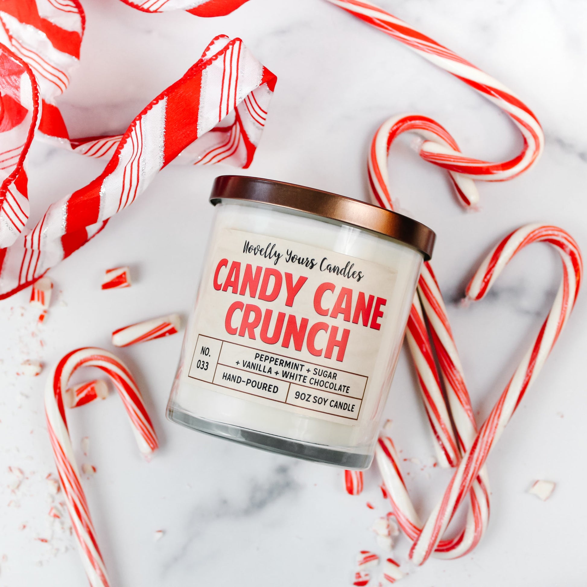 candy cane scented candle in clear glass tumbler jar with bronze lid, surrounded by candy canes