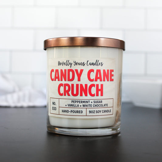 candy cane scented candle in clear glass tumbler jar with bronze lid, on black base with white tile background