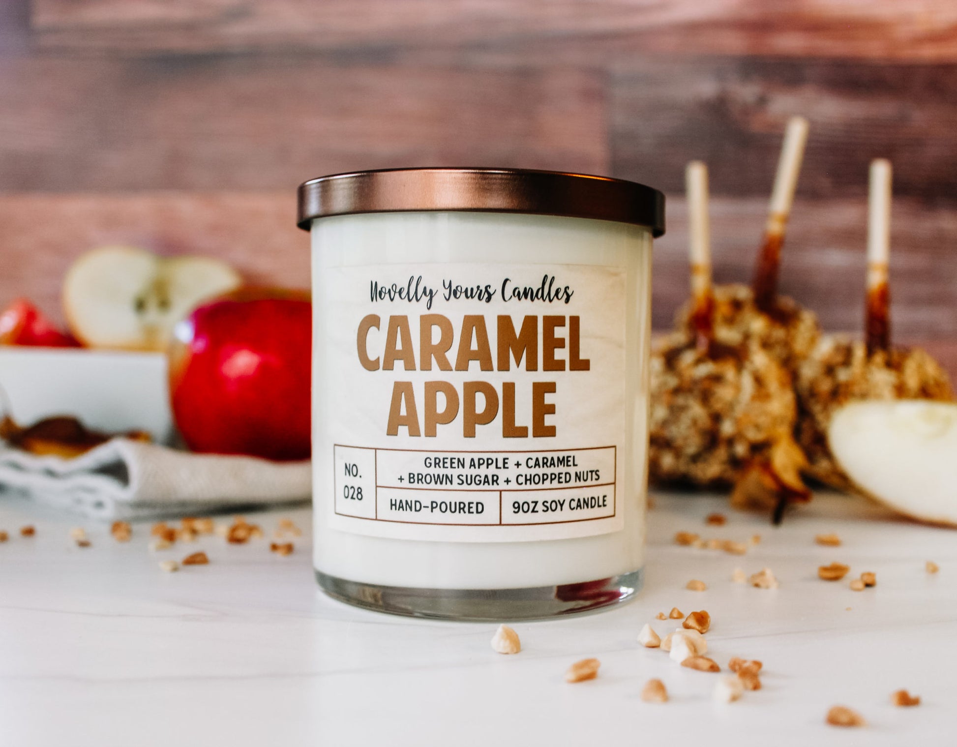 caramel apple scented candle by novelly yours. candle is in clear glass tumbler jar with bronze lid and caramel colored text.