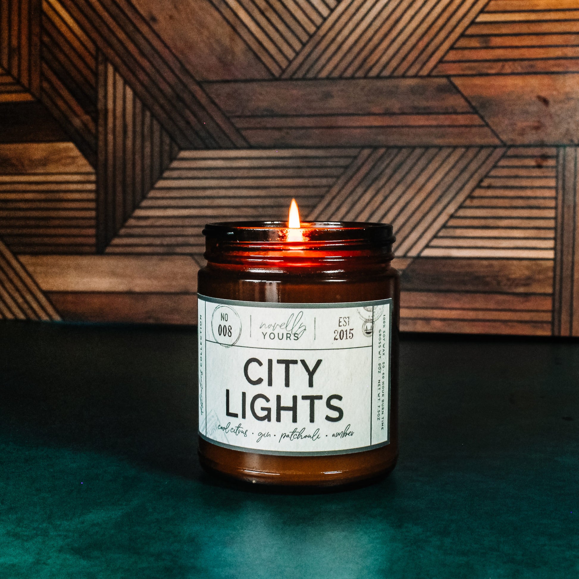 city lights scented soy wax candle in amber jar, lit on jade base with wooden background