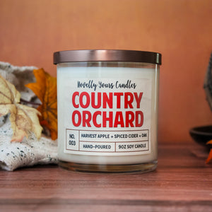 country orchard candle fall seasonal, in glass tumbler jar, surrounded by fall decor on a wood surface with orange background