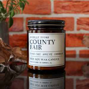 county fair bakery scented soy wax candle in amber jar sits against brick background