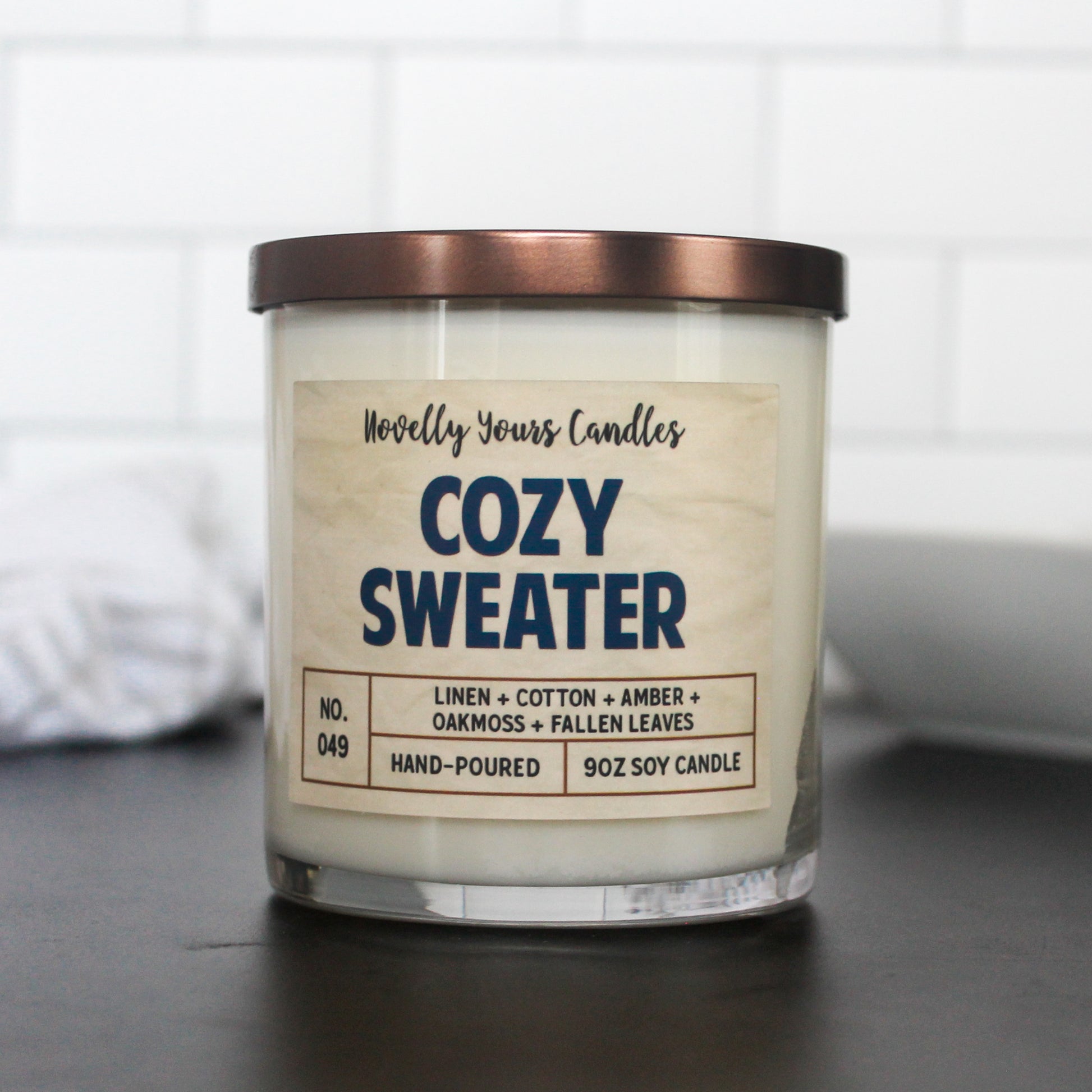 cozy sweater named candle with title in navy blue color. candle sits on black counter with white tile background