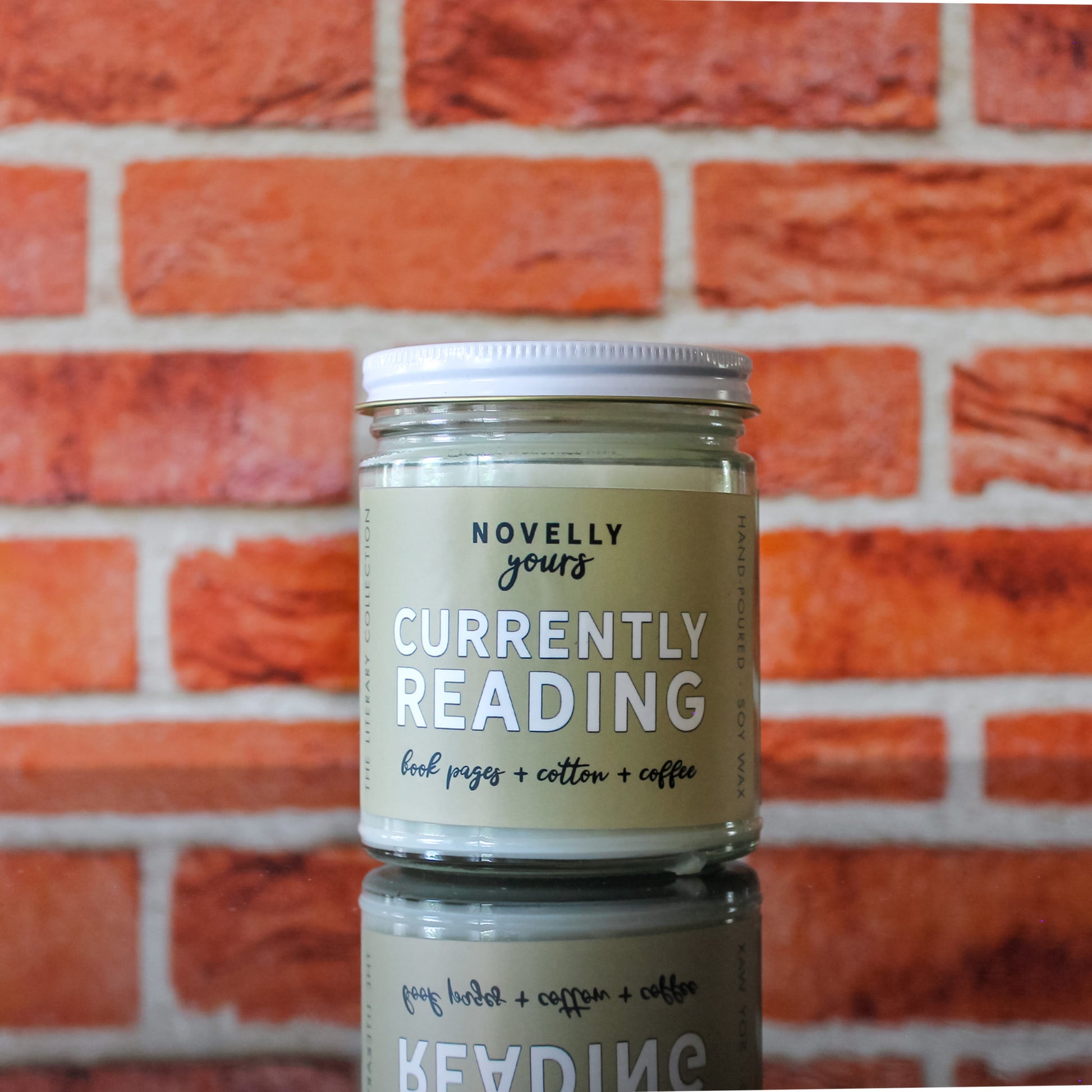 book-themed candle "Currently Reading" with light tan label sits in front of red brick background
