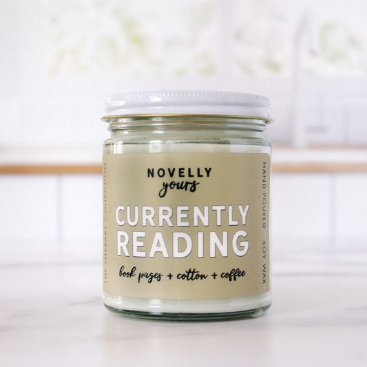 book-themed candle "Currently Reading" with light tan label sits in front of white, clean kitchen background