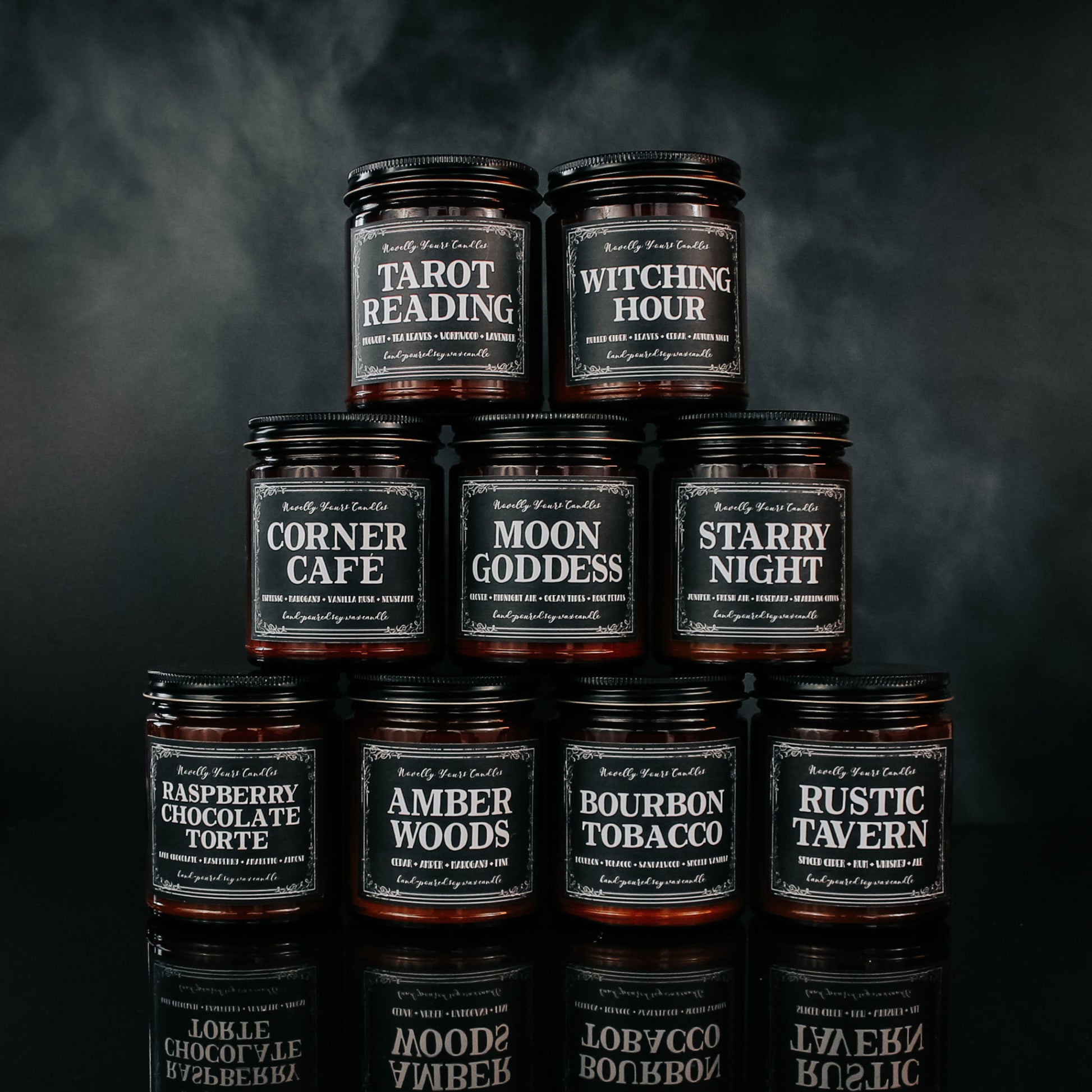 a stack of candles in amber glass jars with black lids and black lids against a smoky black background