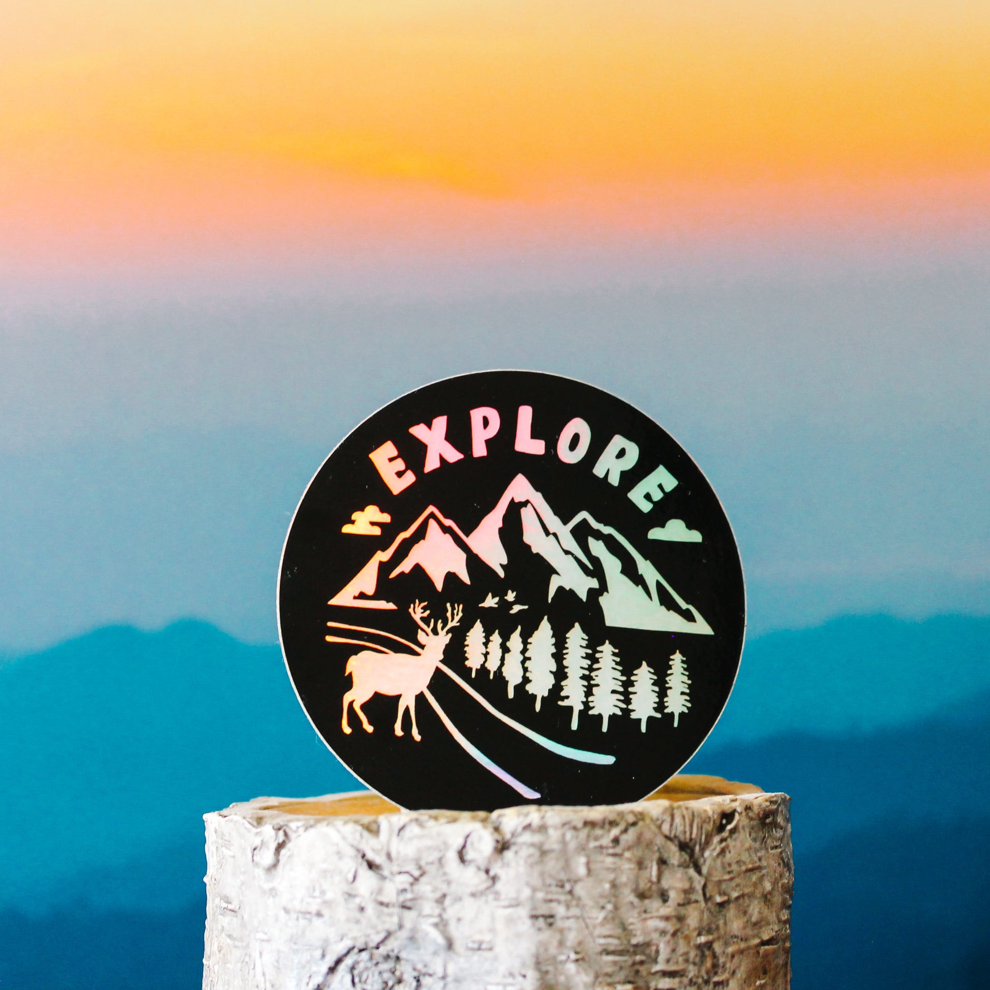 black and rainbow holographic sticker with outdoors and forest scenery with text "explore"