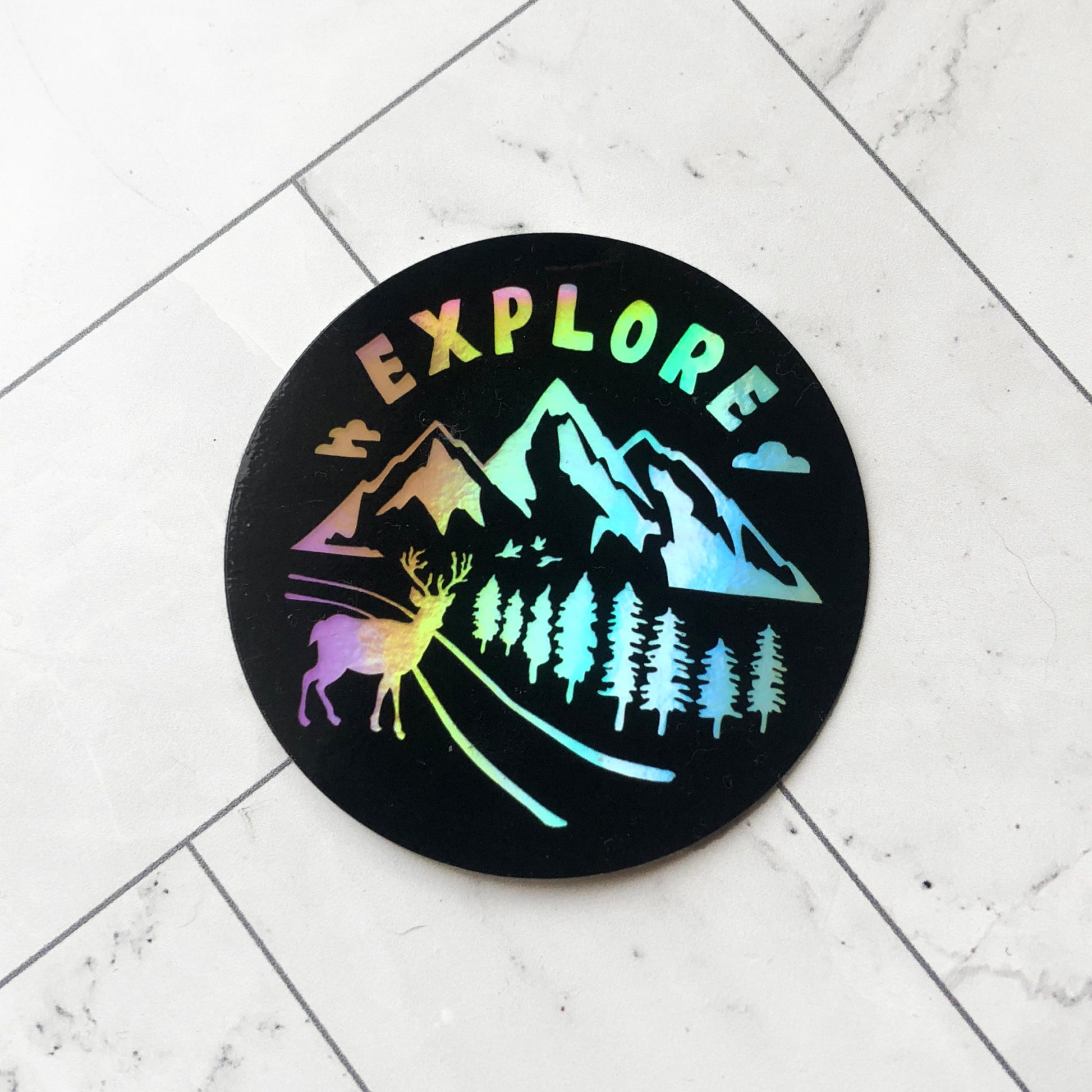 holographic sticker with word "explore" and nature designs of mountains, pine trees, and deer