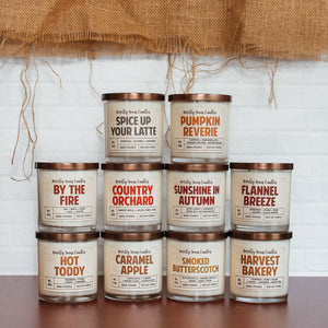 ten fall themed candles made by novelly yours sit stacked on top of each other against a white brick background with a burlap border