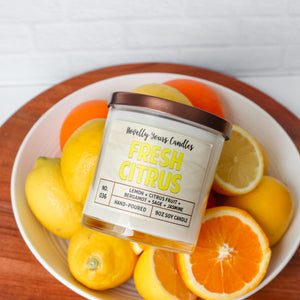 fresh citrus soy wax candle with yellow text in clear glass tumbler with bronze lid. surrounded by oranges and lemons.