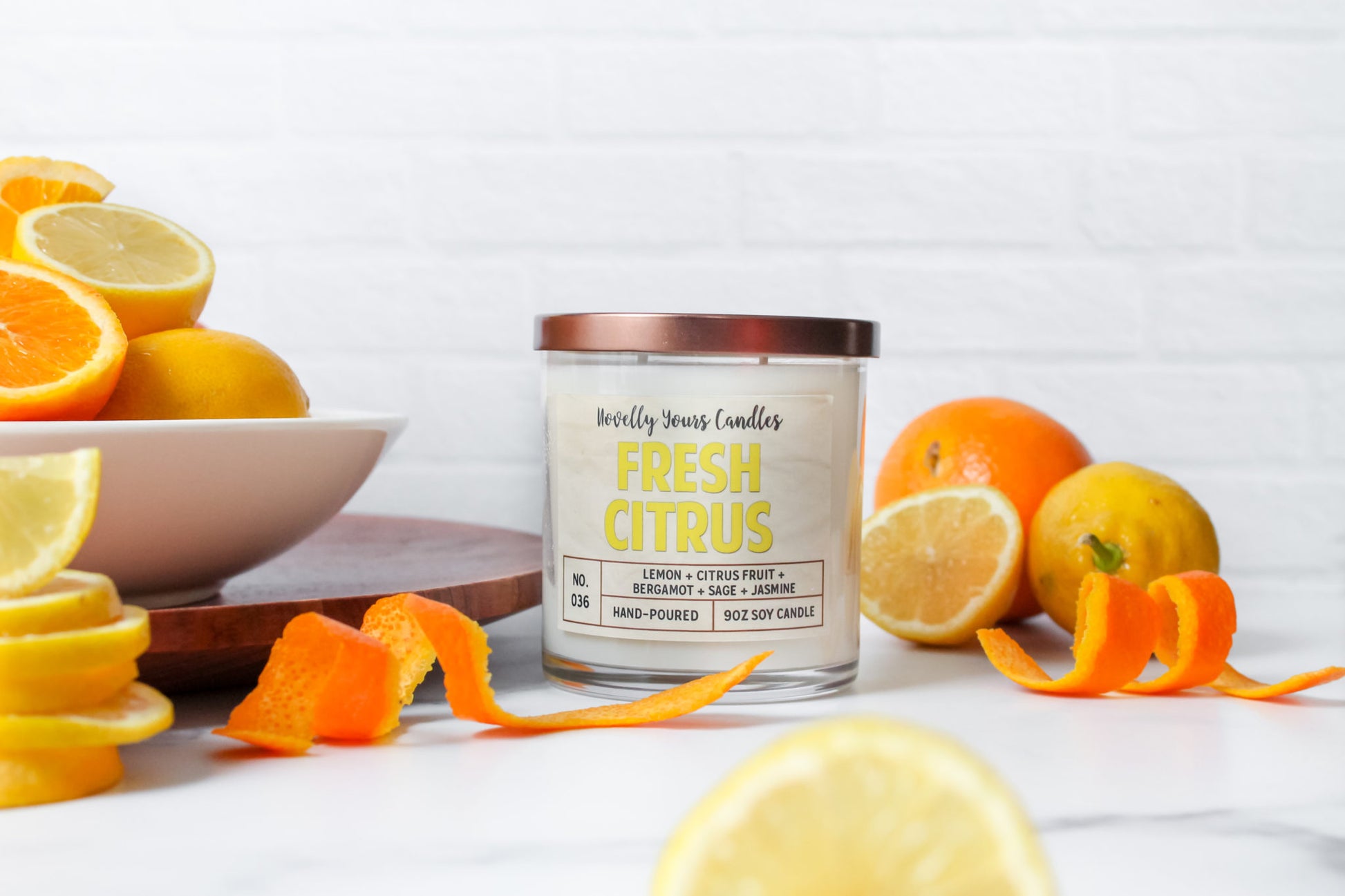 fresh citrus soy wax candle with yellow text in clear glass tumbler with bronze lid. surrounded by oranges and lemons.