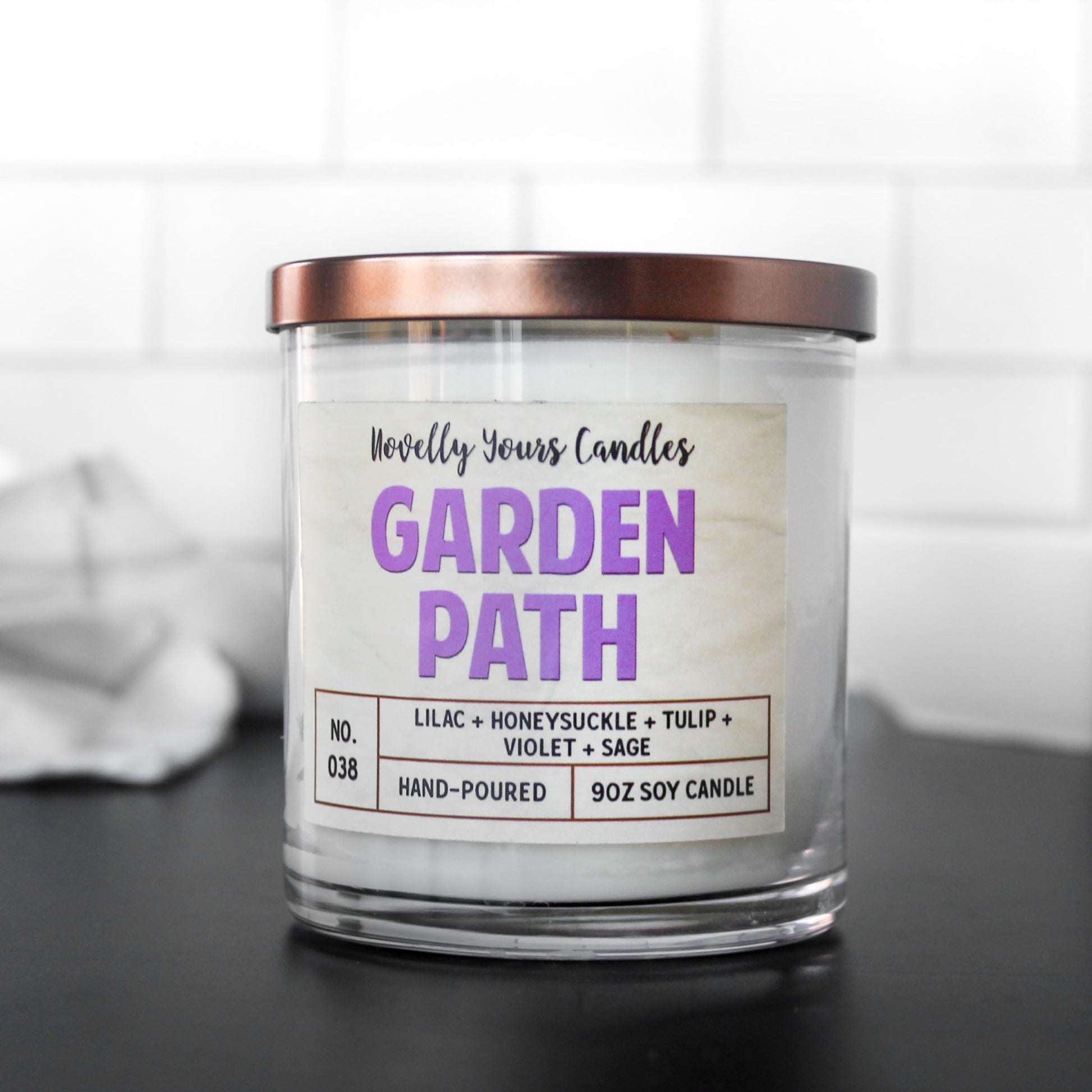 garden path candle with purple text in clear glass tumbler jar with bronze lid