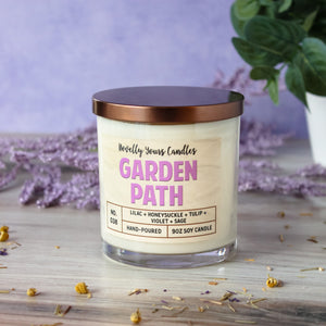 garden path candle with purple text in clear glass tumbler jar with bronze lid