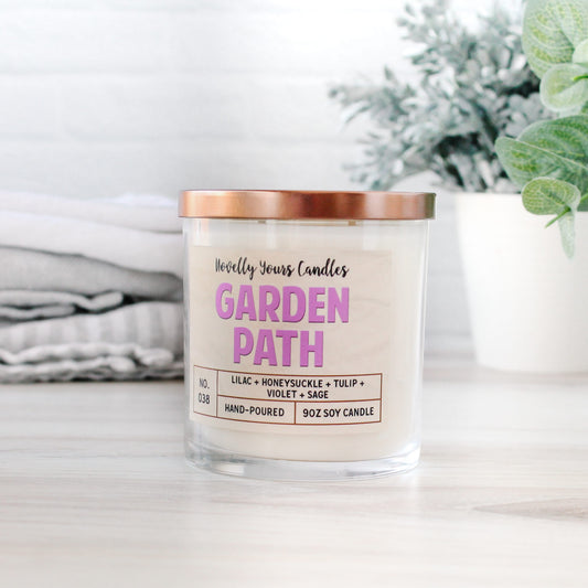 garden path candle with purple text in clear glass tumbler jar with bronze lid