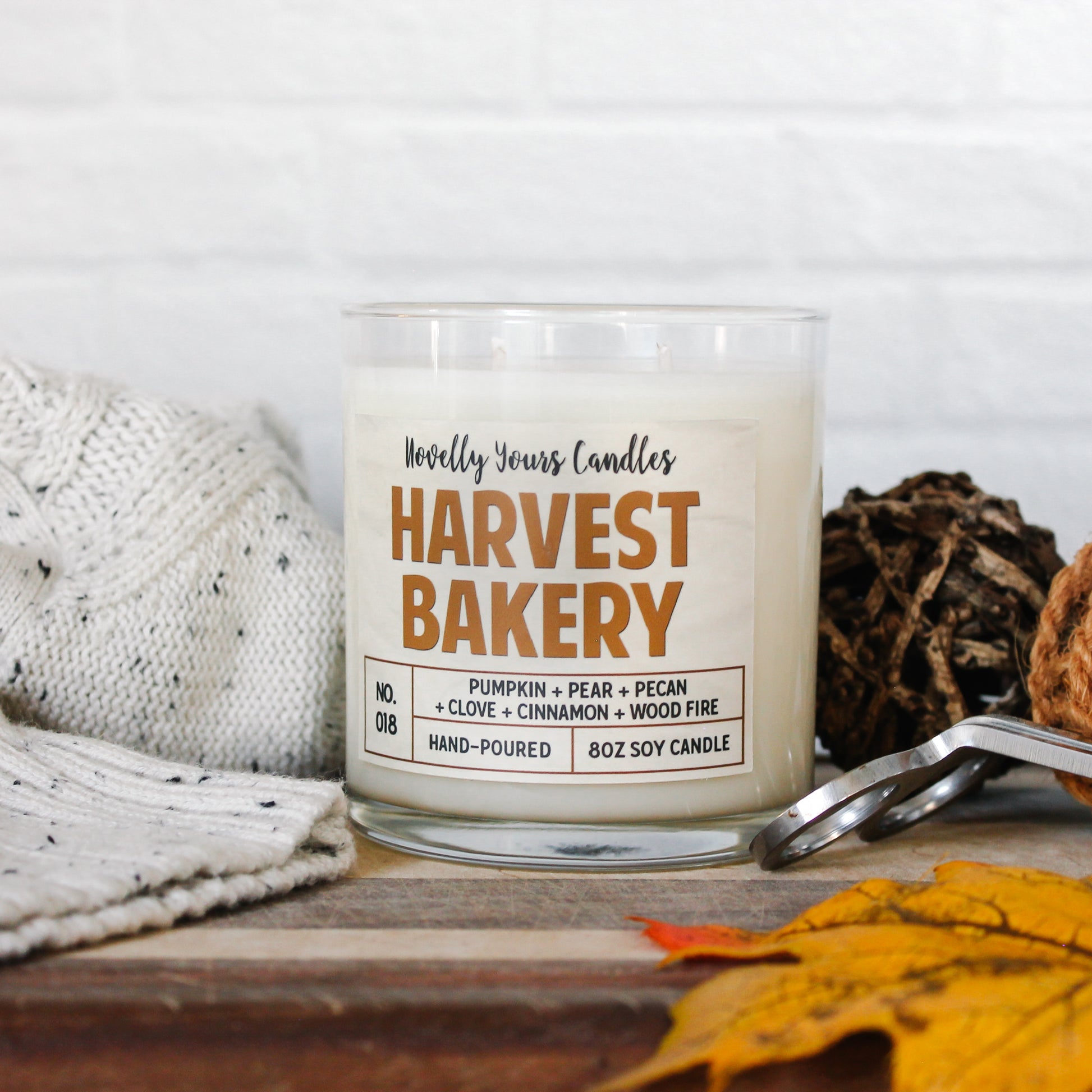 harvest bakery soy wax scented candle in glass tumbler jar. Jar sits on wooden cutting board surrounded by fall decor and a white sweater.