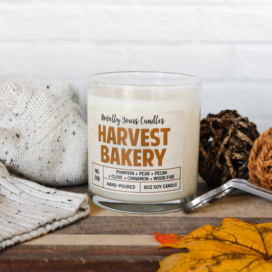 harvest bakery soy wax scented candle in glass tumbler jar. Jar sits on wooden cutting board surrounded by fall decor and a white sweater.