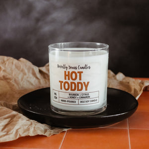 hot toddy soy wax candle in clear tumbler sits on round black plate.