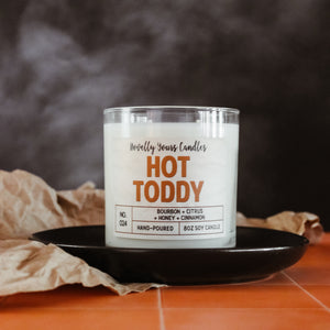 hot toddy soy wax candle in clear tumbler sits on round black plate.