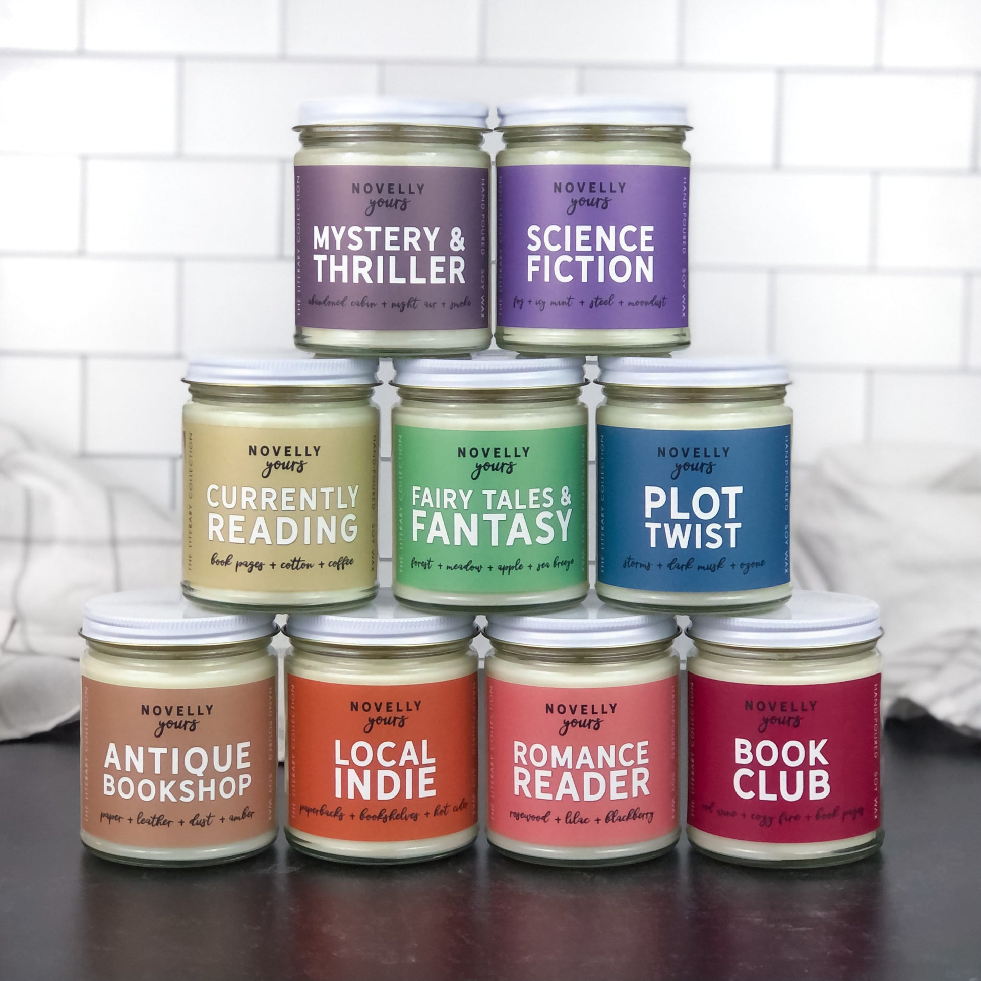stack of book-inspired scented soy wax candles with various colorful labels by novelly yours