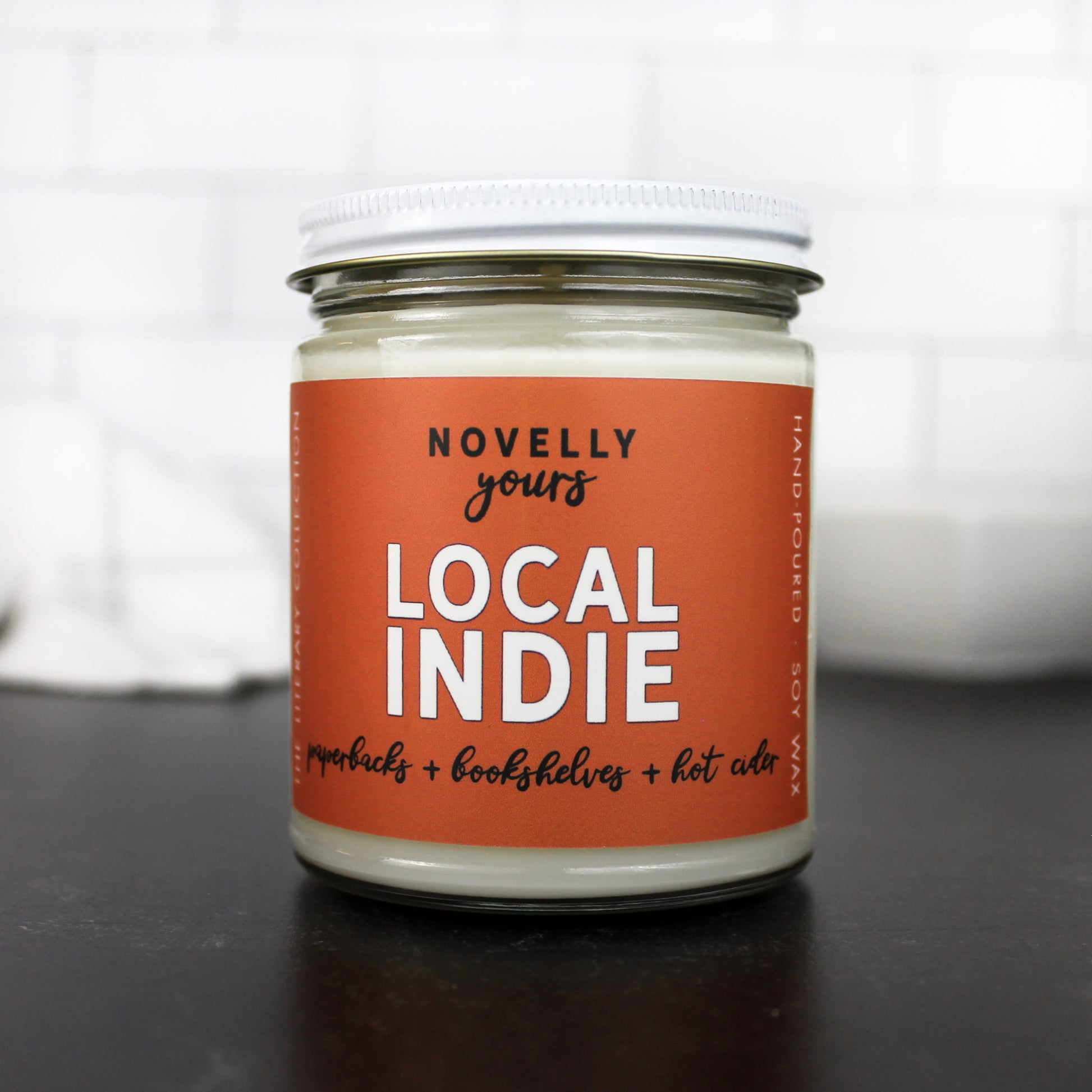 Local indie scented soy wax candle with burnt orange label in clear glass jar with white lid