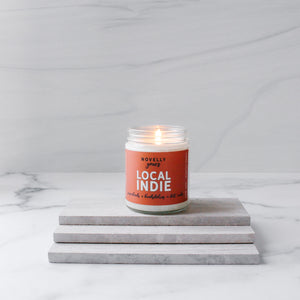 Local indie scented soy wax candle with burnt orange label in clear glass jar with white lid
