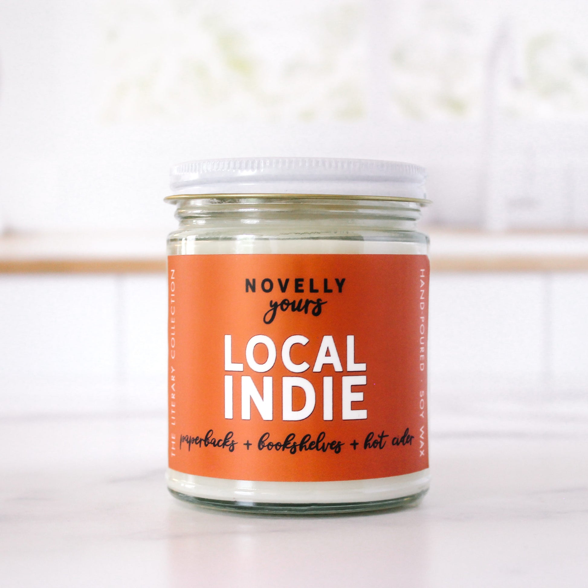 bookish candle "Local Indie" with orange label sits on marble kitchen counter top with clean kitchen in background