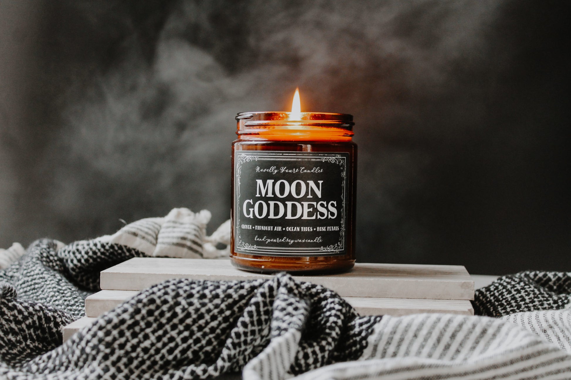 moon goddess scented soy wax candle in amber glass jar, lit surrounded by black and white towel