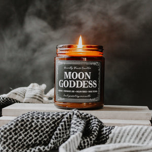 moon goddess scented soy wax candle in amber glass jar, lit surrounded by black and white towel