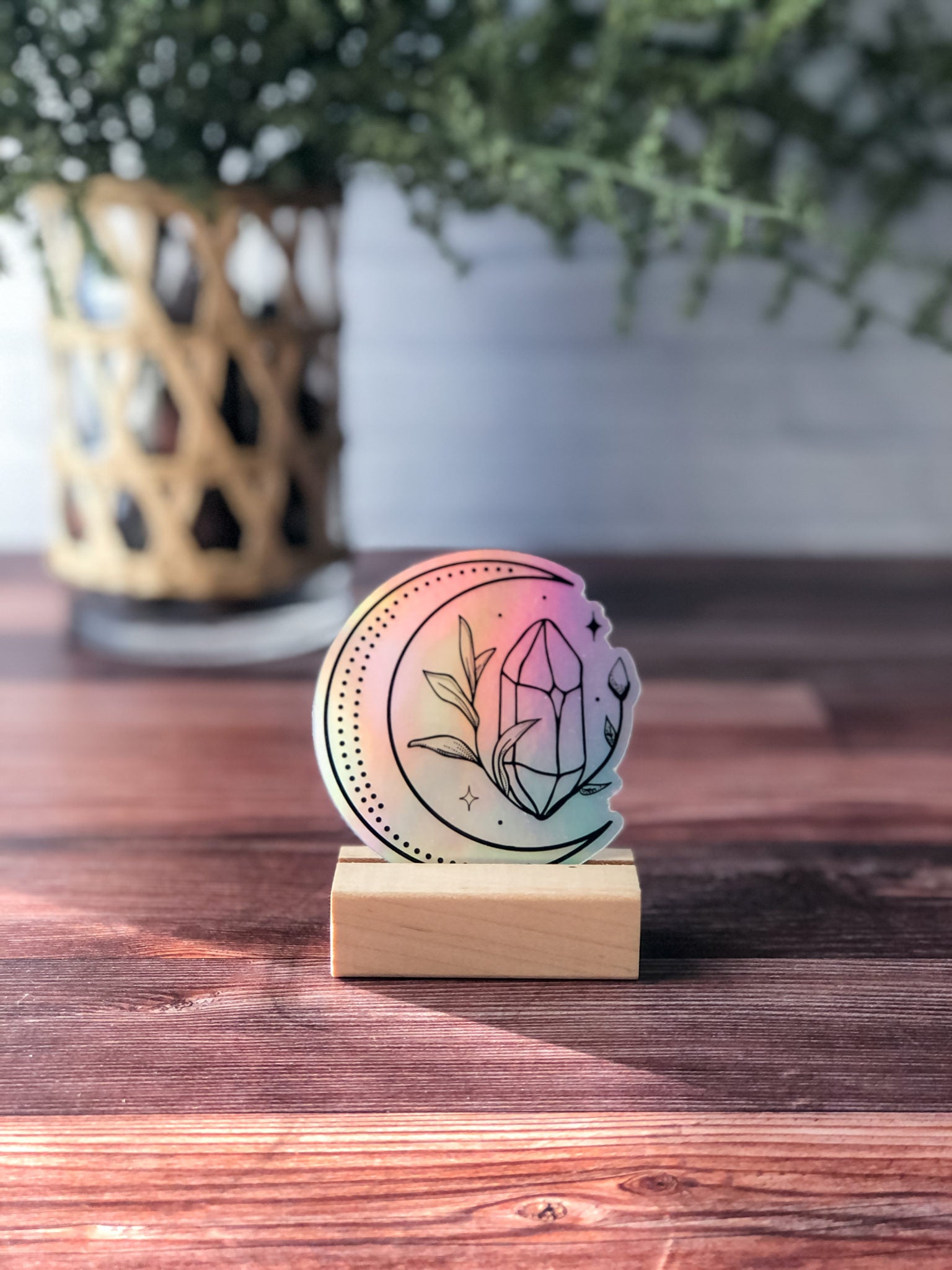 shiny holographic moon & crystal sticker with rainbow iridescent finish. sticker design is crescent moon black outline with crystal, stars, and leafy accents