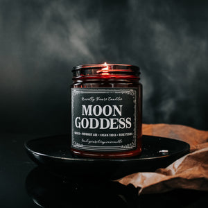 moon goddess scented soy wax candle in amber glass jar, lit on black plate against black backgrounds