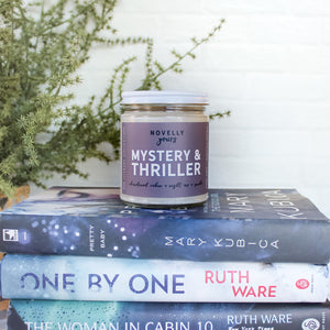 mystery & thriller scented soy wax candle with purple grey label sits on top of mystery books