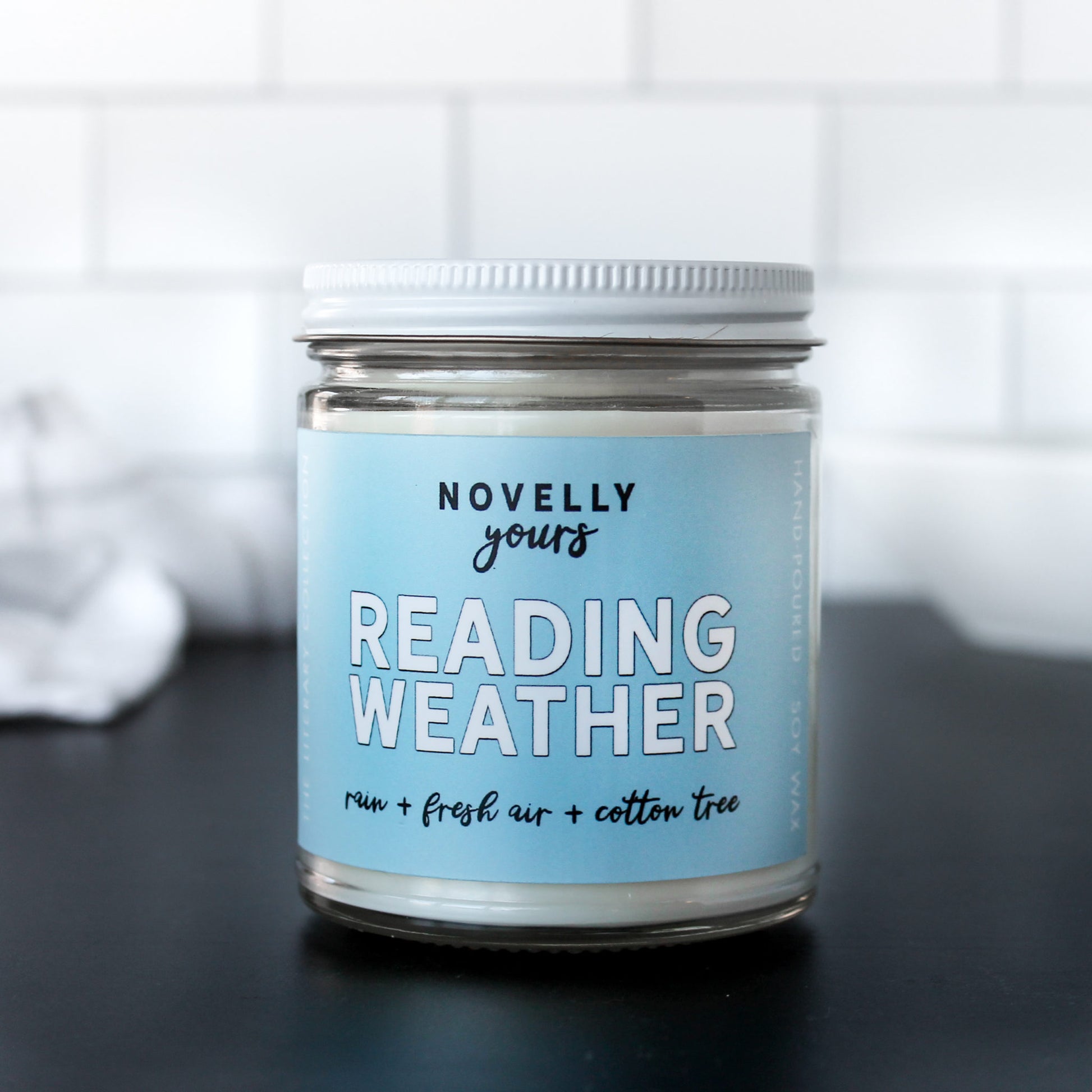 Reading Weather book candle, scented bookish candle made by novelly yours with a light blue label and white metal lid