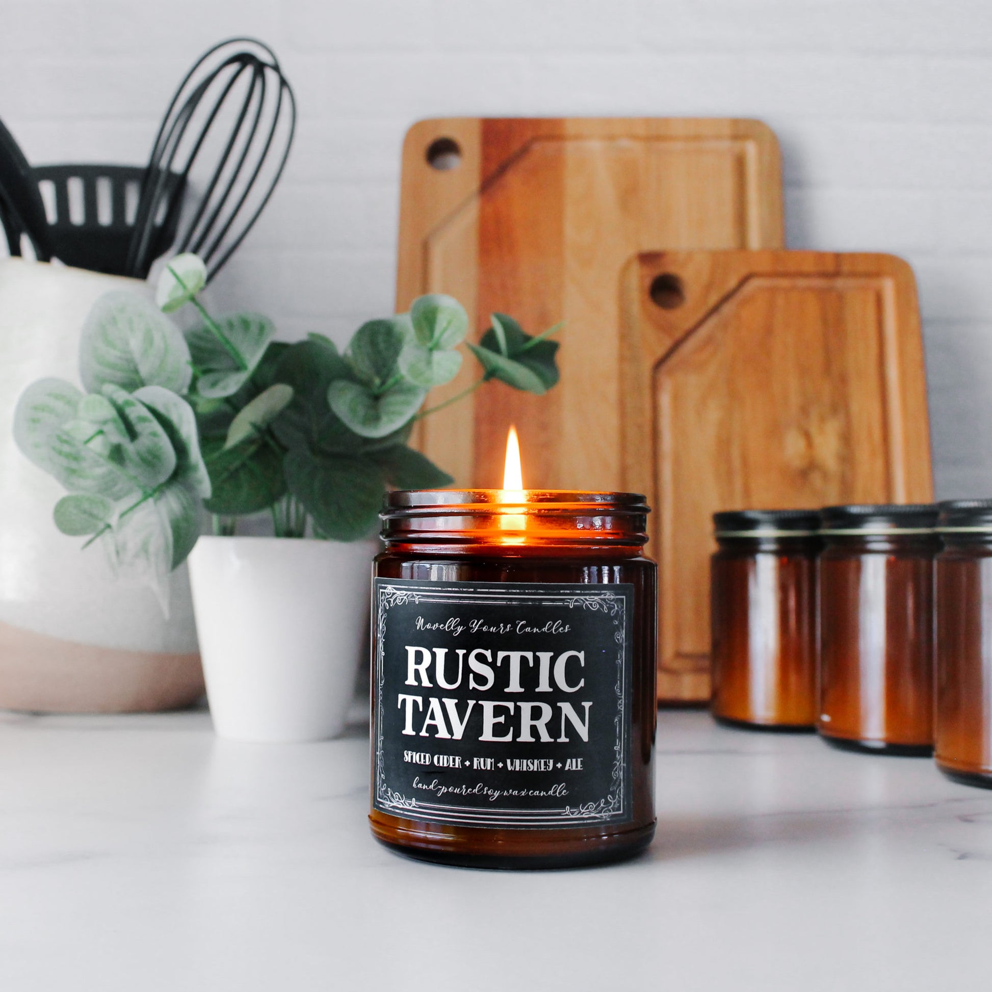 rustic tavern scented soy wax candle in amber jar with black label, lit on marble surface surrounded by kitchen atmosphere