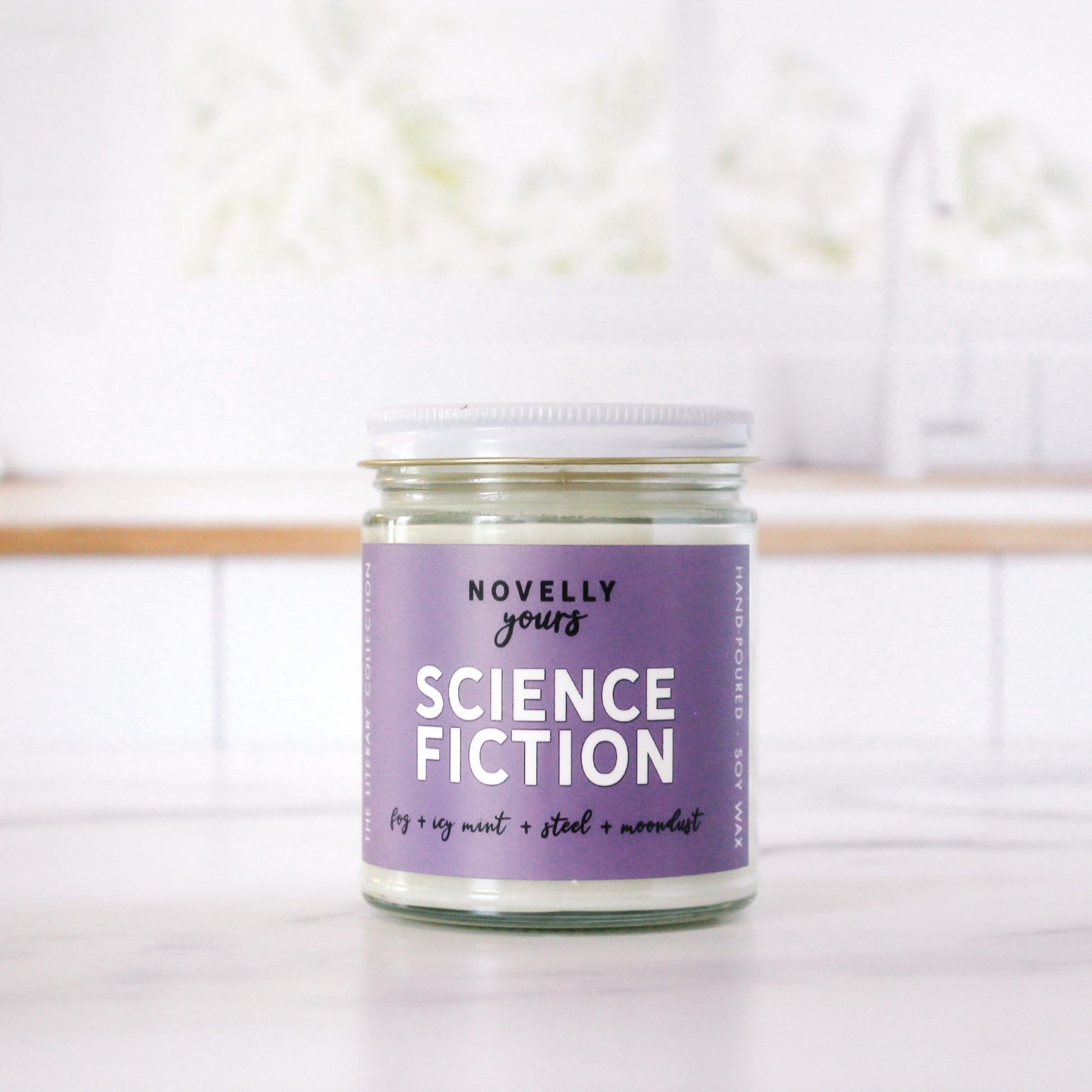 bookish candle labeled "Science Fiction" with purple label sits on a kitchen counter