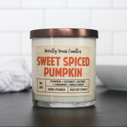 sweet spiced pumpkin candle, name in bright fall orange. candle sits on black surface with white tile background